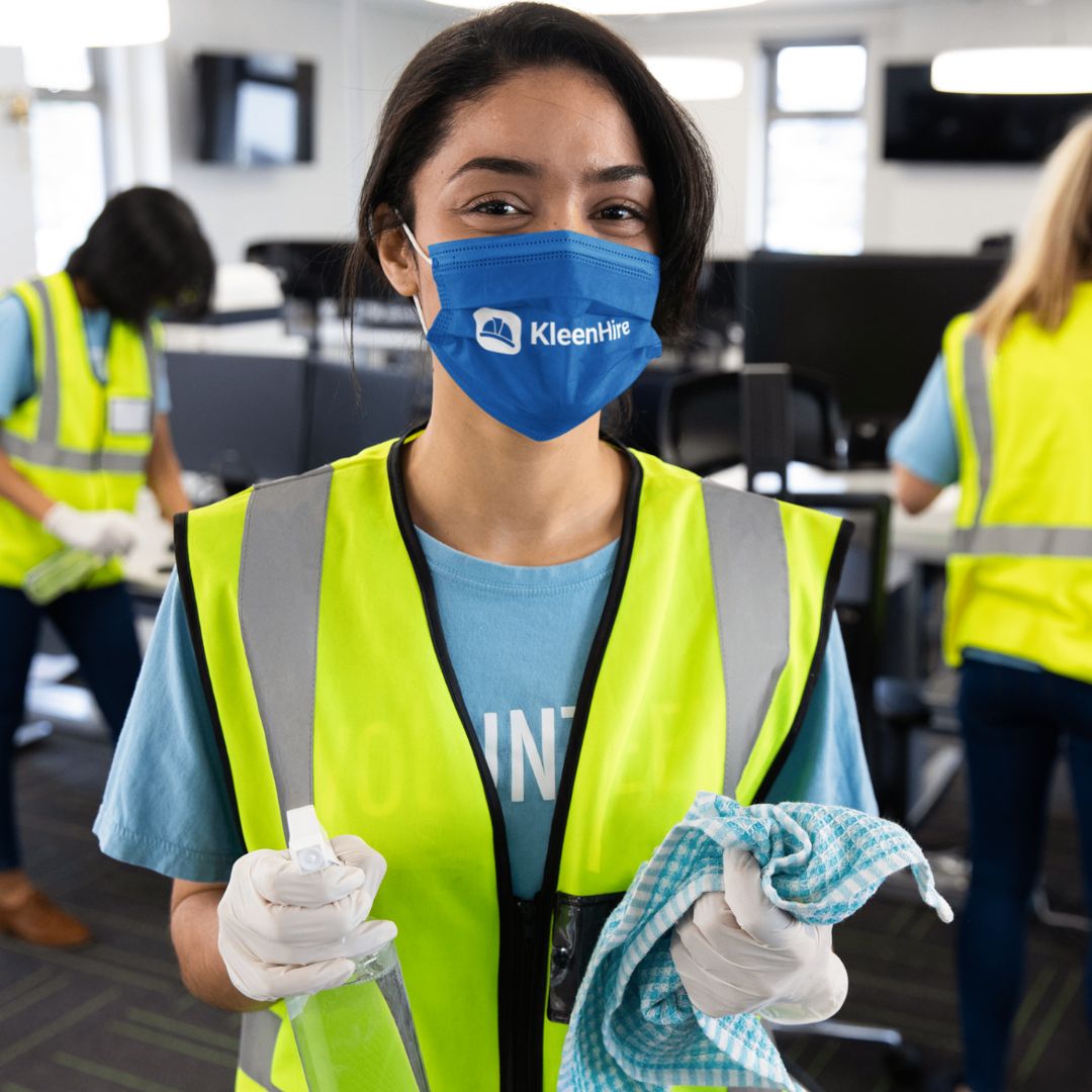 KleenHire branded cleaning staff member in safety vest holding cleaning supplies